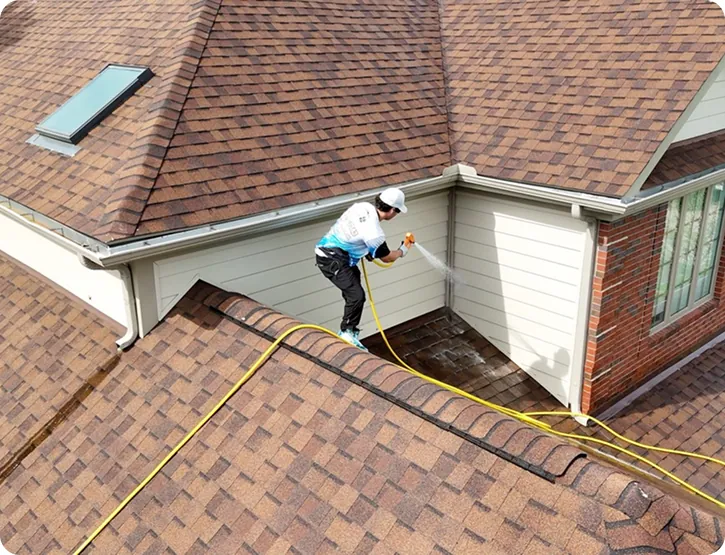Technician soft washing an asphalt-shingle roof with a low-pressure wand